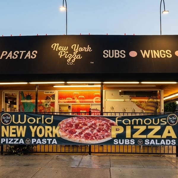 New York Pizza Co. storefront with a black awning listing menu items and a banner advertising "World Famous Pizza."